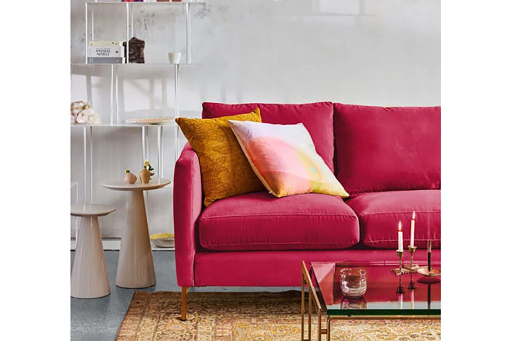 A hot pink couch in a white living room with an orange rug 