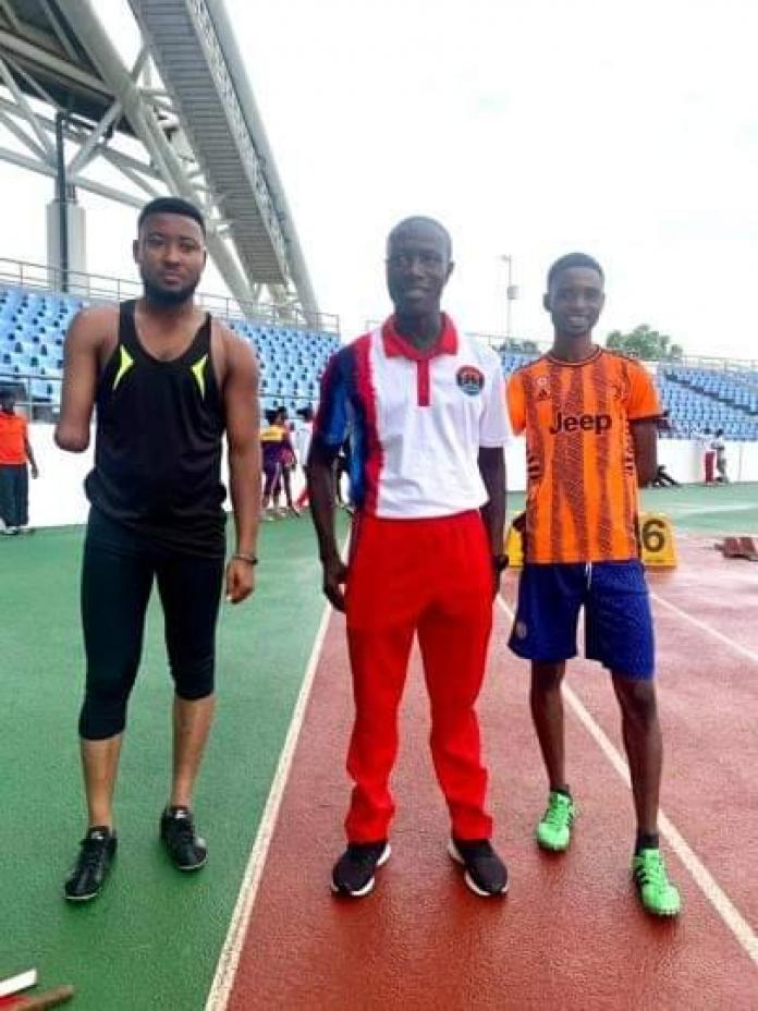 A coach stands on an athletics track, flanked on both sides by male athletes who are missing parts of their right arms.