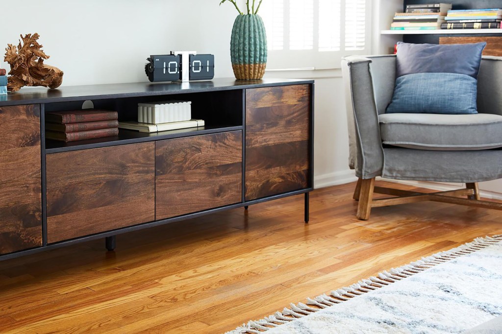 A wood floor and a blue sofa chair in a living room with a brown wood cabinet 