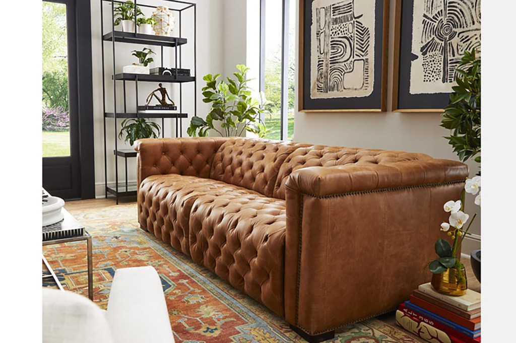 A large brown leather sofa in a nice living room with abstract black and white paintings on the wall and a shelf with knickknacks 