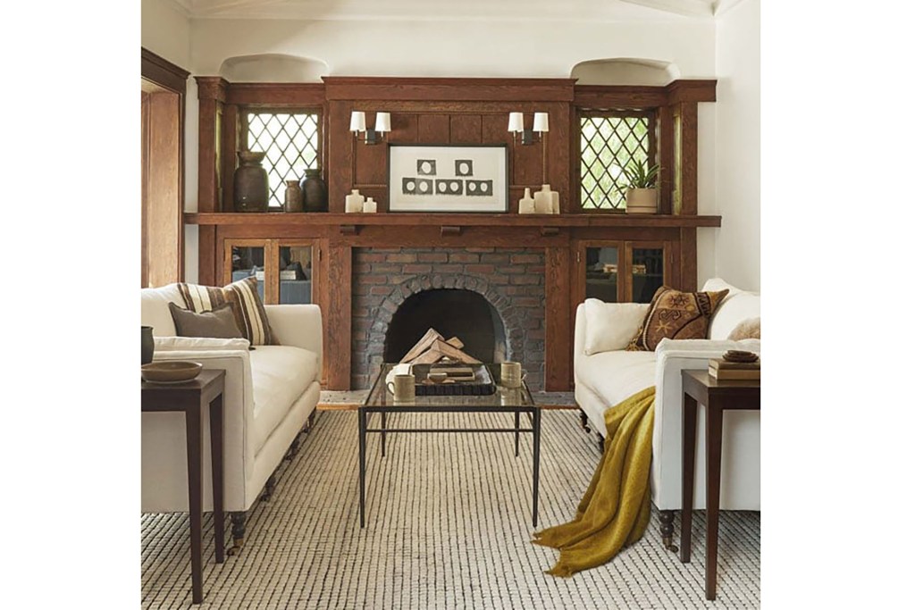 A living room with a brick fireplace and white couches on either side, one with a yellow blanket on it 