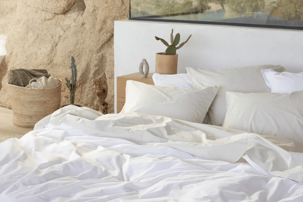 A bed with white beddings and a white headboard against natural colored rock wall 