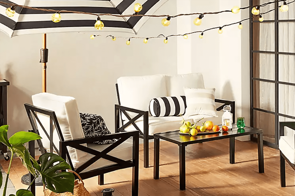 A patio with white furniture and string lights with a glass table 