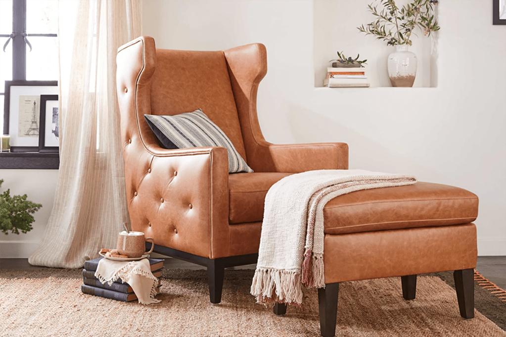 A brown leather chair with a pillow and a blanket over the ottoman