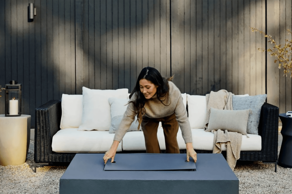 A woman setting up an outdoor fire pit in front of a white couch 